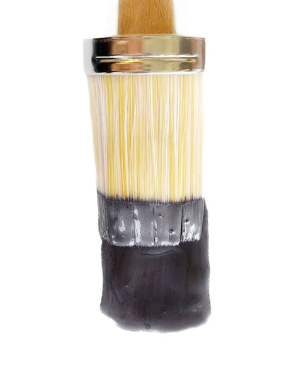 A close-up of a paintbrush with metallic chalk paint in dark purple gray color, showing the bristles and the wooden handle.